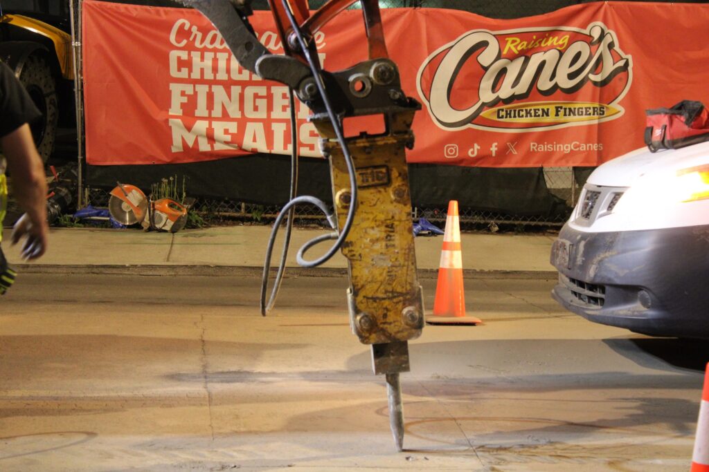 Hydraulic breaker opening the pavement for a utility tie-in on Broadway at night