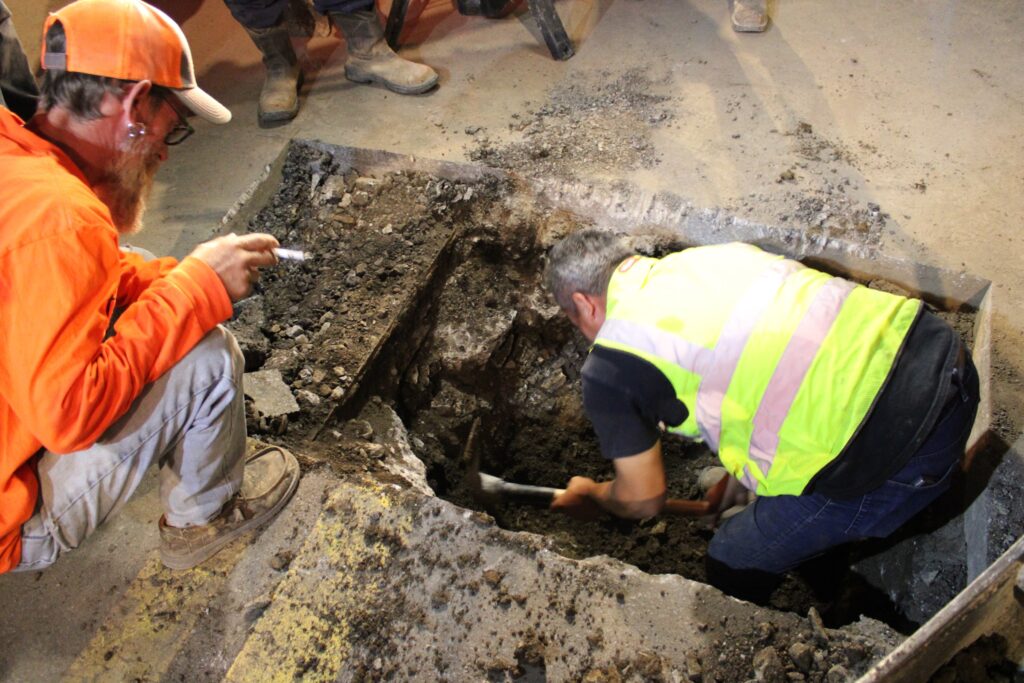 Pipe layer hand-digging around the water main tie-in at Raising Cane's on Broadway